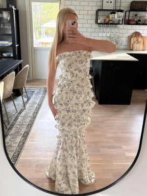 Blommig långklänning med volanger - Populär klänning från Boohoo. Otroligt fin axelbandslös långklänning med blommigt mönster. Klänningen har flera volangdetaljer längs hela längden och en figurnära passform. Jag är 163 cm. Publicerad på flera säljsidor 🌸