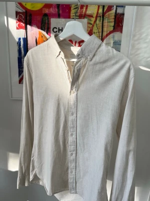 Beige skjorta från Dobber - Stilren beige skjorta från Dobber i bomull. Skjortan har klassisk krage med knappar, långa ärmar och en avslappnad passform. Perfekt för en clean och enkel look.
