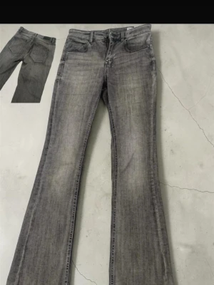 Grå bootcut jeans från Vero Moda - Snygga grå bootcut jeans från Vero Moda med klassisk femficksdesign och dragkedjegylf. Jeansen har en tvättad look och lätt utsvängda ben, perfekta för en trendig och avslappnad stil.