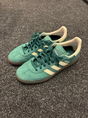 Adidas Spezial gröna sneakers - Snygga Adidas Spezial sneakers i grön mocka med vita detaljer och klassiska tre ränder på sidan. Skorna har lågt skaft, vita innersidor och gummisula. Perfekta för dig som gillar retrostil och streetwear.