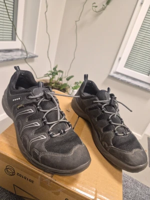 Svarta kängor från Ecco med Gore-Tex 37 - Snygga svarta kängor från Ecco med Gore-Tex-membran och grå detaljer. Skorna har snörning, robust sula och är tillverkade i en kombination av läder och textil. Perfekta för dig som vill ha både stil och funktion i vardagen.