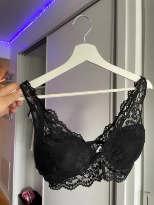 Svart spets-bh med breda axelband - Snygg svart bh i spets med breda axelband och vacker blomspets runt kuporna. Bh:n har bygel och ger bra stöd, perfekt för dig som gillar en feminin och stilren look. Materialet är mjukt och stretchigt för extra komfort.