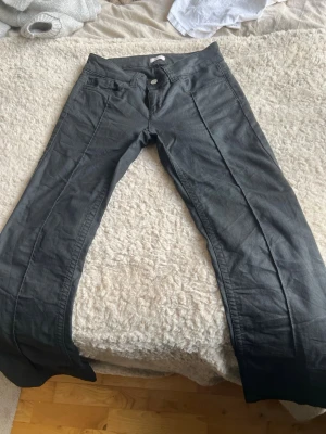 Nelly byxor - Säljer ett par svarta jeans med utsvängda ben och klassisk femficksdesign. Jeansen har knapp- och dragkedjestängning samt markerade sömmar framtill. Perfekta för dig som gillar en trendig och avslappnad stil.