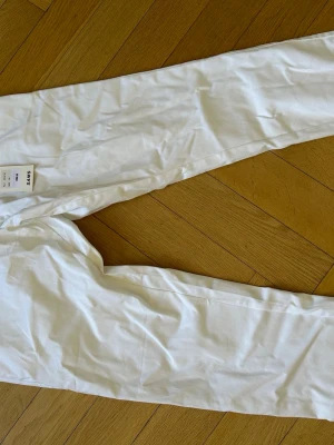 Vita chinos, Oanvända Etikett kvar - Vita chinos från med rak passform och klassisk look. Byxorna är tillverkade i ett lätt och mjukt material som ger en fräsch och stilren känsla. Perfekta för dig som gillar minimalistisk och clean stil. Etikett kvar oanvända. NYPRIS 899kr