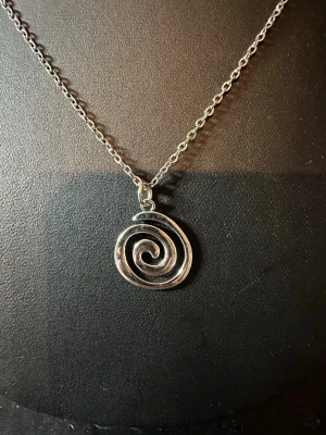 Silverfärgat halsband med spiralhänge - Snyggt halsband i silverfärg med ett unikt spiralformat hänge. Kedjan är tunn och stilren, vilket gör att spiralhänget verkligen står ut. Perfekt för dig som gillar minimalistisk och modern design. Materialet ser ut att vara metall.