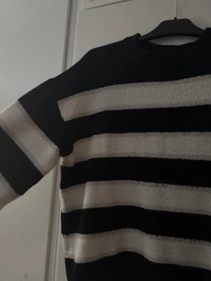 Svartvit randig stickad tröja - Säljer en oversized stickad tröja med breda svarta och vita horisontella ränder. Tröjan har rund halsringning och långa ärmar. Materialet känns mjukt och mysigt, perfekt för kyligare dagar. Passar dig som gillar en avslappnad och trendig stil.