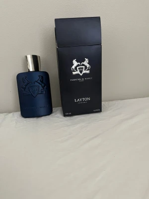 Parfums de Marly Layton 125ml - Parfums de Marly Layton är en lyxig parfym i en snygg mörkblå flaska med silverfärgad kork. Flaskan har en elegant, matt finish och pryds av märkets ikoniska logga. Kommer i originalförpackning. Volym: 125 ml.