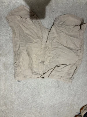 Beige linneshorts från Kappahl, storlek M - Snygga beige shorts från Kappahl i storlek M. De har klassisk passform med knapp och dragkedja framtill samt praktiska fickor på sidorna. Perfekta för varma dagar och enkla att matcha med olika outfits.