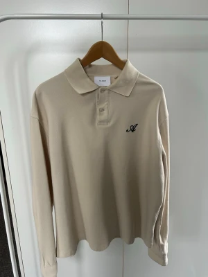  Axel Arigato Pikéskjorta  - Stilren beige långärmad pikéskjorta från Axel Arigato med klassisk krage och knäppning framtill. Storlek M. Ett set tillsammans med ett par shorts som går att köpa i annan annons. 