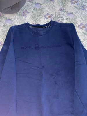Blå Sail Racing sweatshirt - Mörkblå sweatshirt från Sail Racing med rund halsringning och diskret logga broderad på bröstet. Tröjan har långa ärmar och är tillverkad i mjukt material, perfekt för en avslappnad stil. Tvättar innan jag fraktar om du som köpare vill 