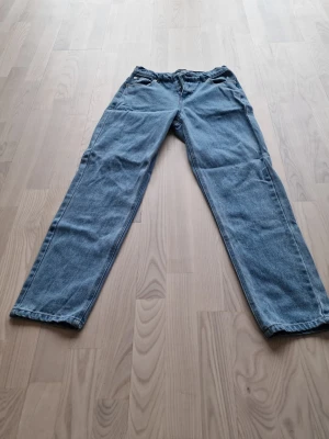 Blå raka jeans i klassisk modell - Säljer ett par blå jeans i klassisk rak modell med fem fickor och normal midja. Jeansen har en tidlös tvätt och är tillverkade i denim. Perfekta för en avslappnad och stilren look. Det är storlek 176 men sitter som typ W28.
