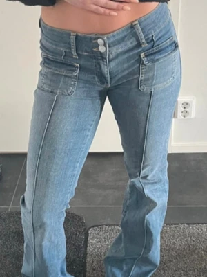 Blå bootcut jeans med fickdetaljer - Snygga blå bootcut jeans med dubbla knappar i midjan och markerade sömmar framtill. Jeansen har två stora fickor framtill. Observera att färgen är i andra bilden ‼️