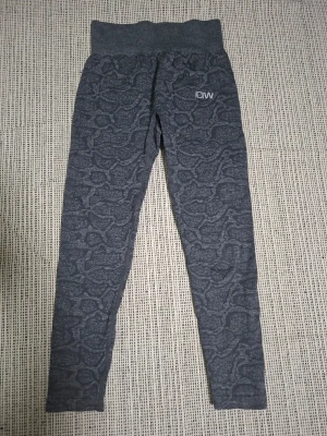 Mörkgrå mönstrade leggings från ICANIWILL. Seamless tights graphite. - Snygga mörkgrå leggings från ICANIWILL med diskret ormmönster och hög midja. Stretchigt material som sitter tajt och bekvämt, perfekt för träning eller chill. Logga på vänster höft. Materialet känns mjukt och följsamt.