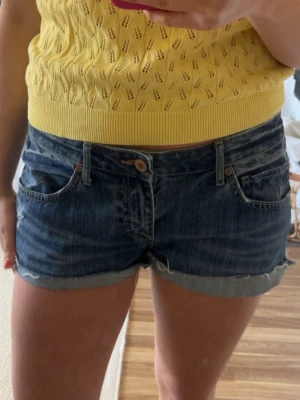 Blå jeansshorts - Snygga blå jeansshorts med upprullad kant och klassisk femficksdesign. Shortsen har normal passform och stängs med knapp och dragkedja. Perfekta för varma sommardagar och enkla att matcha med olika toppar.