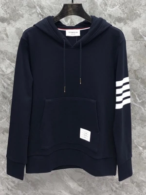 Mörkblå hoodie med vita ränder - Stilren mörkblå hoodie från Thom Browne med klassiska vita ränder på ena ärmen och en praktisk känguruficka framtill. Justerbar huva med dragsko och diskret etikett på fickan. Perfekt för en avslappnad och trendig look.