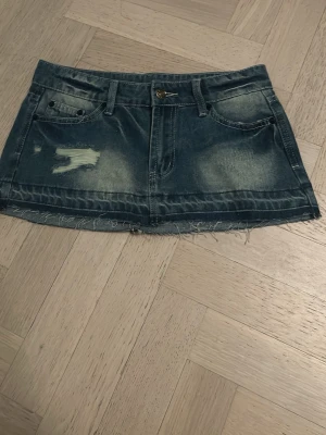Blå jeanskjol med slitningar - Cool blå jeanskjol med slitna detaljer och fransig nederkant. Klassisk femficksmodell med bälteshällor och knappstängning framtill. Perfekt för en avslappnad och trendig look. Köpte på marknad i Spanien förra sommaren och passar tyvärr inte längre💕skulle säga att de är xs i storlek men står att det är s
