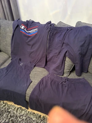 Mörkblått loungewear-set Champion - Tvådelat loungewear-set från Champion i mörkblått. Setet består av en t-shirt med tryckt logga i vitt, rött och blått samt ett par mjuka byxor med dragsko i midjan. Perfekt för chill hemma eller avslappnade dagar.