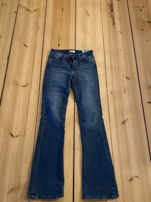 Blå bootcut jeans från ONLY - Snygga blå bootcut jeans från ONLY med klassisk femficksdesign och dragkedjegylf. Jeansen har en lätt tvättad look och utsvängda ben, sliten vid fötterna. 