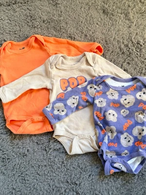 3-pack långärmade bodys, So Cute, 62 cm - Tre långärmade bodys för baby från So Cute. En i orange, en beige med POP-tryck och en blå med moln och texten POP. Alla i mjuk bomull och med tryckknappar i grenen. Perfekt för små barn 0-3 månader.den orangea har några små märken efter smakprov men jag har inte testat att få bort dom, skickar därför med en extra body (sista bilden) 