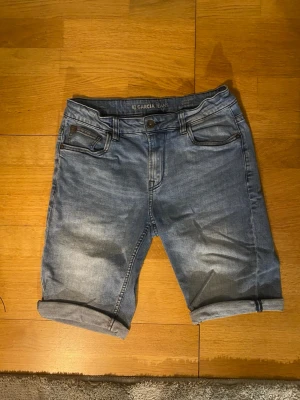 Blå jeansshorts från Garcia Jeans - Snygga blå jeansshorts från Garcia Jeans med klassisk femficksdesign och uppvikta benslut. Shortsen har normal passform och är tillverkade i bomull med en lätt tvättad look. Perfekta för en avslappnad stil under varmare dagar.