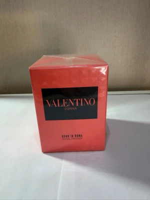 Valentino Donna Born In Roma parfym - Valentino Donna Born In Roma Coral Fantasy är en parfym i en snygg, korallröd kartong med svart och guld text. Förpackningen är rektangulär och tillverkad av kartong. Perfekt för dig som gillar exklusiva och trendiga dofter.