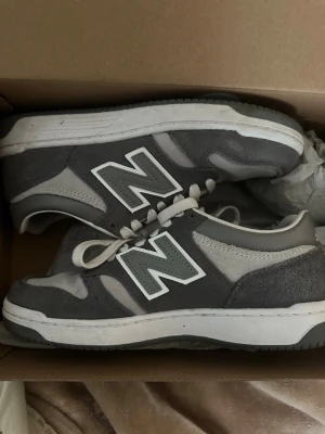Grå New Balance sneakers i mocka - Snygga grå sneakers från New Balance med klassisk vit N-logga på sidan. Skorna har ovandel i mocka och mesh, vita skosnören och en vit och grå sula. Använt bara två gånger så de är som nya.