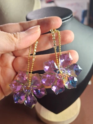 Lila blommiga statementörhängen - Unika örhängen med stora blommor i lila och blått, tillverkade av glittrande akryl. Hängande på guldfärgade kedjor med små strassdetaljer. Perfekt för dig som vill sticka ut med färg och glamour.