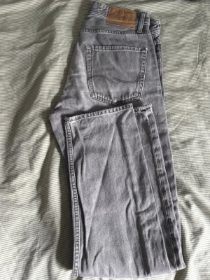 Grå jeans från Jack & Jones - Säljer ett par grå jeans från Jack & Jones med klassisk femficksmodell och raka ben. Jeansen har en snygg tvättad look och detaljerad bakficka med broderad söm. Tillverkade i mjuk denim som är skön att bära.