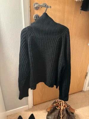 Svart stickad polotröja - Säljer en svart, chunky stickad polotröja med bred ribbad krage och lång ärm. carig oversized fit och grovstickat mönster sopm ger en cool och avslappnad vibe. Perfekt för kalla dagar och enkel att styla till jeans eller kjol.