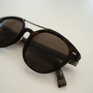 Ermenegildo Zegna | Solglasögon - Solglasögon från Ermenegildo Zegna i klassisk rund form med mörkbruna tortoise-bågar. Modellen är EZ0006 med polariserade glas som ger bra komfort och minskar reflexer. Storlek 51-20-145. Stilren design med metallbåge över näsan och metallskalmar som ger en elegant och tidlös look. Glasögonen är använda men i gott skick. Originalfodral/box medföljer. Inköpta på Dubai Mall år 2017.