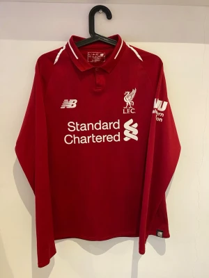 Liverpool Långärmad 2018/19 – New Balance – S - Äkta Liverpool långärmad matchtröja från säsongen 2018/19.  Storlek S. Mycket bra skick – inga fläckar, hål eller slitage. New Balance‑modell med Standard Chartered‑sponsor och Western Union‑patch.