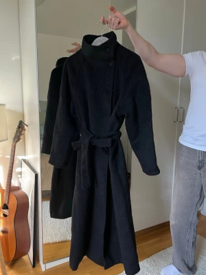 Lång kappan med hög halsen - Stilren svart lång rock med hög krage och knappar vid halsen från Nelly, Perfekt på våren och hösten!