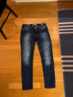 Mörkblå jeans med slitningar - Säljer ett par mörkblå jeans med snygga slitningar och tvättade detaljer framtill. Klassisk femficksmodell med knapp- och dragkedjegylf. Jeansen har smal passform och är tillverkade i stretchigt denimtyg för extra komfort.