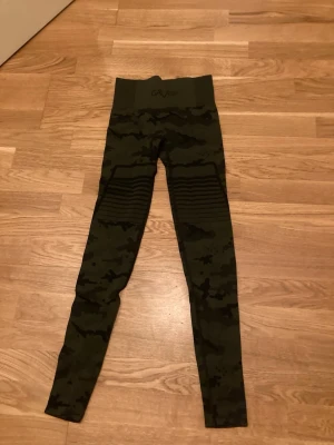 Camo tights från Gavelo stl S - Snygga tights från Gavelo i grönt camomönster. Hög midja med ribbad kant och logga framtill. Stretchigt material som sitter skönt och följer kroppen, perfekta för gymmet eller löpning.Nya!!!