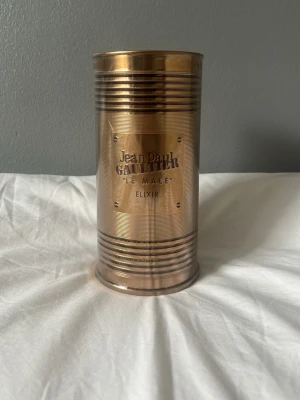 Jean Paul Gaultier Le Male Elixir - Jean Paul Gaultier Le Male Elixir parfym i en metallisk, cylindrisk guldfärgad burk med räfflade detaljer. Märkets logga och parfymens namn är ingraverade på framsidan. Förpackningen har en unik och lyxig design som sticker ut. Den är helt oöppnad! Pris kan diskuteras vid snabb affär!
