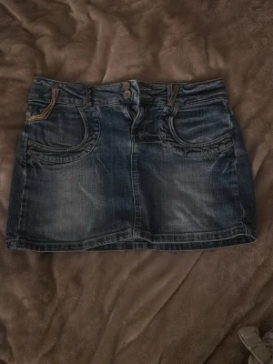 Mörkblå jeanskjol från Big Star - Snygg mörkblå jeanskjol från Big Star med klassiska fickor fram och bak, dubbla knappar i midjan och slitna detaljer. Perfekt för dig som gillar en cool och avslappnad stil. Kjolen har kontrastsömmar och en kort passform.