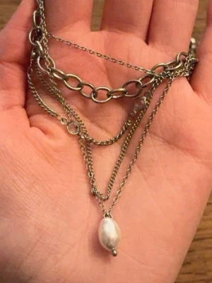 Silverfärgat halsband med pärla - Säljer ett snyggt multilager halsband i silverfärgad metall med olika kedjor och en vit pärla som hängsmycke. Kedjorna har både grova och tunna länkar vilket ger ett coolt och trendigt uttryck. Perfekt för att lyfta din outfit.🥹🧸🩷