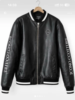 Svart skinnjacka Icono Couture - Snygg svart skinnjacka från Icono Couture med vita detaljer och tryck på ärmar och rygg. Jackan har dragkedja framtill, två fickor och ribbade muddar i svartvitt. Perfekt för dig som gillar streetwear och vill sticka ut med en unik look.