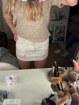 Vit kort jeanskjol med slitningar - Säljer en vit kort jeanskjol med slitna detaljer framtill. Kjolen har klassisk femficksdesign och rå kant nedtill för en trendig look. Perfekt att matcha med en stickad tröja eller crop top.