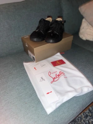 Svarta Christian Louboutin sneakers - Snygga svarta sneakers från Christian Louboutin i mocka med vit broderad logga på hälen. Klassisk låg modell med svarta skosnören och diskret design. Kommer med originalkartong och dustbag. Perfekta för dig som vill ha något exklusivt och stilrent.