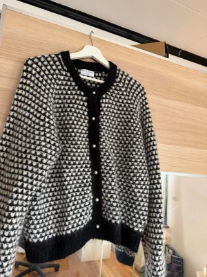 Svartvit star pattern kofta Holly & Whyte - Säljer en fluffig svartvit kofta från Holly & Whyte by Lindex med pärlknappar framtill. Koftan har ett grafiskt mönster, rund halsringning och ribbade muddar. Perfekt för lager på lager och riktigt mysig till hösten.