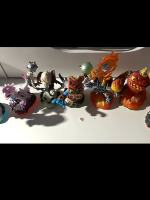 Skylanders-figurer samling - Säljer en samling Skylanders-figurer i plast med olika färger och former. Figurerna har detaljer som eld, vingar, svärd och rustningar. Färgerna är blandade, bland annat lila, orange, blå, grön och röd. Perfekt för dig som gillar samlarprylar eller vill komplettera ditt Skylanders-spel.