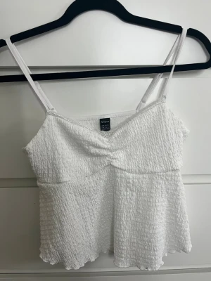 Vit sommartopp - Söt vit sommartopp från SHEIN med smala axelband och lätt rynkad struktur. Toppen har en twistad detalj framtill och är tillverkad i ett material som känns som ett mjukt syntetmaterial. Perfekt till sommaren och enkel att styla med olika looks.