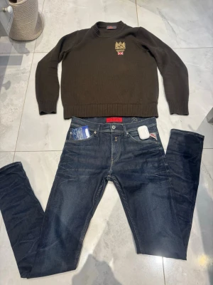 Mörkblå jeans från Replay - Snygga mörkblå jeans från Replay med klassisk femficksdesign och röda detaljer på fickan. Jeansen har raka ben och är tillverkade i denim med tydliga sömmar. Perfekta för en trendig och avslappnad stil.