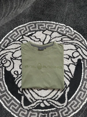 Olivgrön Sail Racing t-shirt - Snygg olivgrön t-shirt från Sail Racing med diskret logga broderad på bröstet. Klassisk rund hals och korta ärmar. Tillverkad i mjuk bomull som känns skön mot huden. Perfekt för dig som gillar stilrena och sportiga plagg.