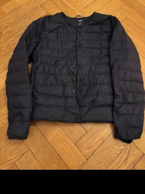 Svart dunväst från Uniqlo Ultra Light Down - Snygg svart dunväst från Uniqlo Ultra Light Down med knäppning framtill. Västen är tunn och lätt, perfekt för lager på lager och har en stilren, minimalistisk design utan krage. Tillverkad i ett mjukt, quiltat material med dunfyllning. Frågor?? Kontakta mig innan ni beställer