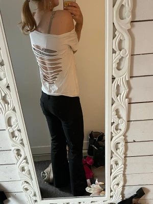 Vit offshoulder t-shirt med slitsar - Vit t-shirt med offshoulder-design och korta ärmar. Baksidan har flera horisontella slitsar som ger en edgy look. T-shirten är i bomull och har en loose passform, perfekt för en avslappnad stil.