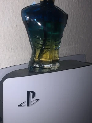 Jean Paul Gaultier Le Male parfym - Säljer en Jean Paul Gaultier Le Male parfym i den ikoniska flaskan formad som en manlig torso. Flaskan har en snygg blå-grön-gul färgskiftning och är tillverkad i glas. Perfekt är en klassiker för dig som gillar unika doftflaskor. Skulle gissat att det är ungefär 80-95 ml kvar.