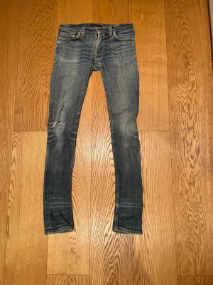 Blå skinny jeans från Nudie Jeans - Säljer ett par blå skinny jeans från Nudie Jeans med slitningar och otroligt snygga fade detaljer. Jeansen har klassisk femficksmodell, låg midja och smal passform. Materialet är mjukt denim i bomull och bakfickorna har Nudie Jeans signatursöm. Enda minuset på dem här jeansen är att de är slitna, det finns hål på flera platser men de är lättlösta. Passar perfekt för någon som siktar på ett par lite tightare jeans som har snygga fade detaljer. Pris kan diskuteras så var inte rädd att fråga!🙋 