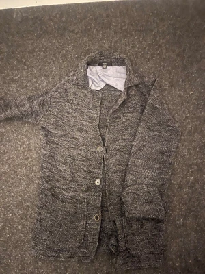 Grå stickad kofta från Mavi - Mysig grå stickad kofta från Mavi med knappar framtill och två stora fickor. Koftan har en klassisk krage och är perfekt för lager-på-lager-stil. Materialet är grovstickat och ger en avslappnad vibe.